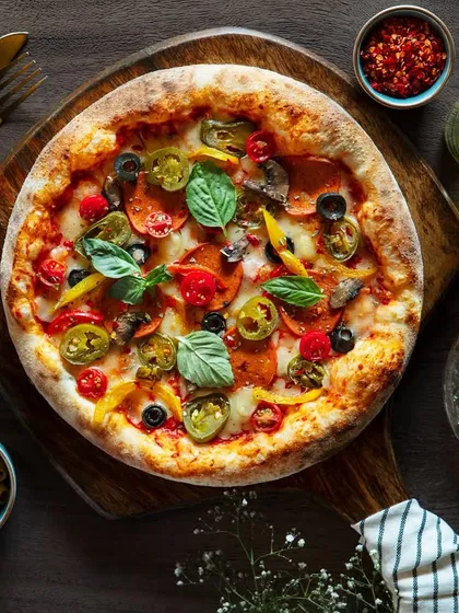 A classic pepperoni pizza, photographed from directly above for The Khyber Resort's menu. This flat lay style allows all the toppings like jalapeños, olives, and basil to be clearly visible, making for a mouthwatering shot.