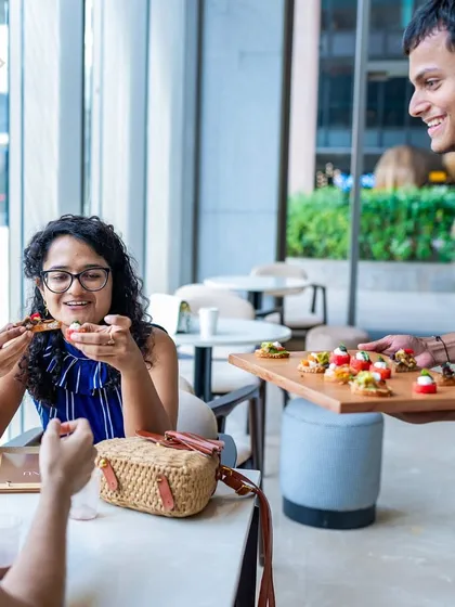 A server presenting a tray of canapés to a smiling customer at our RMZ Ecoworld location. We love to delight our guests.