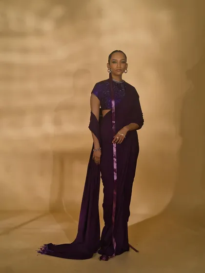 A classic lookbook shot from the 'Amethyst Edit'. The simple, standing pose provides a clear and unobstructed view of the purple draped saree, perfect for a designer's catalogue.