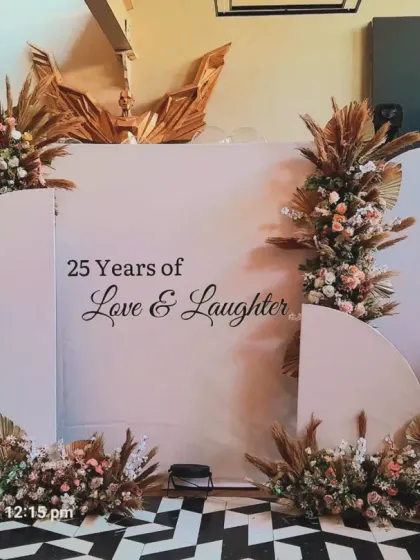 A modern and elegant backdrop celebrating "25 Years of Love & Laughter." The design uses clean arched panels and is decorated with boho-style pampas grass and floral arrangements.