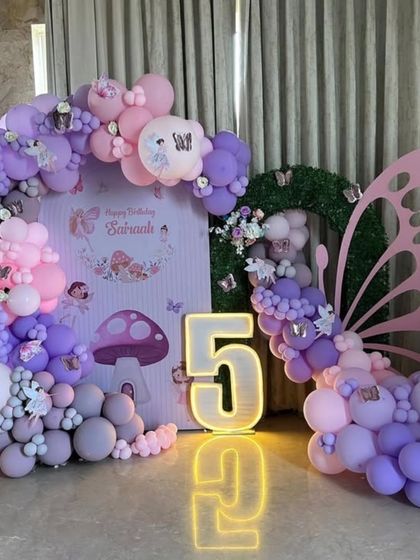 An enchanted forest theme for Saanvi's 5th birthday. The decor features a large butterfly wing made of balloons, mushroom props, and a light-up number "5".