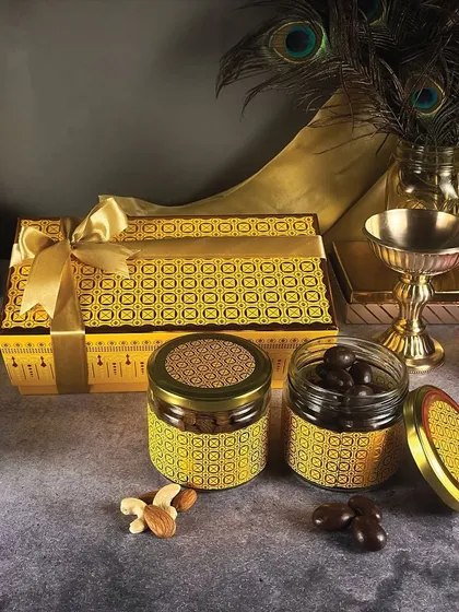 The 'Snack it up' gift box is a vibrant and festive option. It features a patterned yellow box and matching jars filled with delicious chocolate-coated nuts and dry fruits.