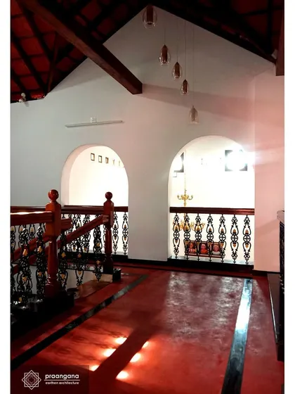 The upper floor hallway with its polished red oxide floor reflecting the light. The arches provide a glimpse into the rooms, creating a sense of depth and connection.