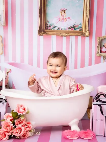 A baby girl enjoys a "spa day" in a glamorous pink-themed setup, complete with a miniature bathtub and shopping bags. This fun and sassy shoot is perfect for celebrating a little fashionista's personality.