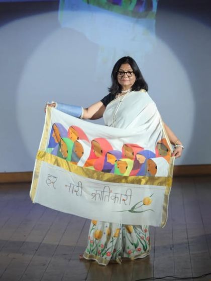 Here I am on stage, displaying my hand-painted saree with the theme "Har Nari, Krantikari" (Every Woman is a Revolutionary). The pallu features portraits of women, celebrating their power to bring change.