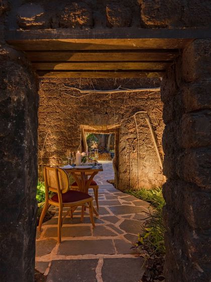 An intimate dining nook set within the ancient stone ruins of the Sanctuary Bar & Kitchen in Goa. The design uses the historic architecture as a dramatic backdrop, creating a unique and romantic dining experience.