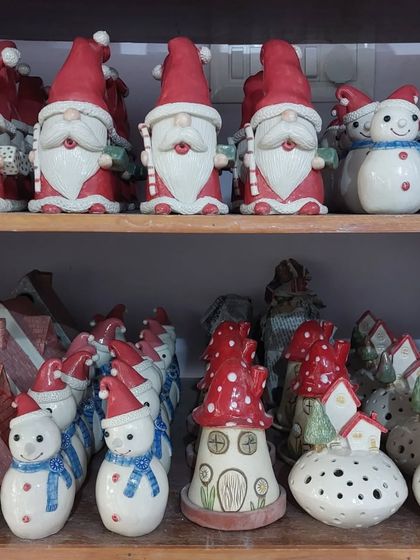A shelf in my studio packed with Christmas goodies, including gnomes, snowmen, and mushroom fairy houses, all waiting to be packed for markets and online orders.