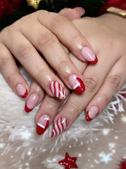 A classic Christmas manicure with red French tips, candy-cane stripes, and cute Santa hat accent nails. It's the perfect festive look.