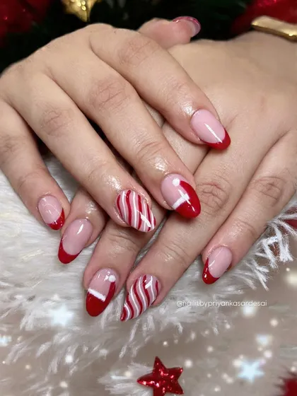 A classic Christmas manicure with red French tips, candy-cane stripes, and cute Santa hat accent nails. It's the perfect festive look.