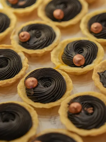 Miniature chocolate tarts with a swirl of dark chocolate ganache and a copper-dusted hazelnut.