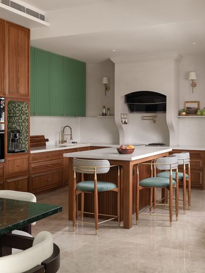 The dry kitchen at Tinted Tapestries features a large island with seating, perfect for casual entertaining. We used a mix of warm wood and sage green cabinetry, with houndstooth-upholstered bar stools adding a classic pattern.