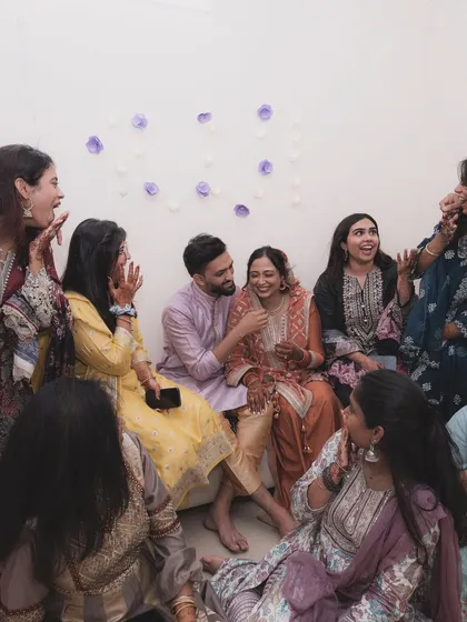 A candid shot of a couple surrounded by friends and family during a pre-wedding gathering. The room is filled with laughter and joy, capturing the essence of celebration.