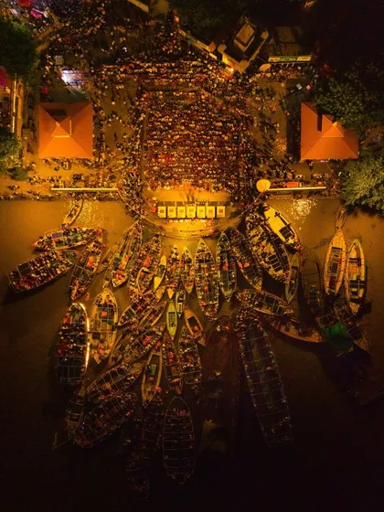 A top-down aerial view of the Ganga Aarti in Varanasi, capturing the spiritual gathering as a symphony of light. The boats filled with devotees and the priests on the ghat create a powerful image of collective faith, visible only from this unique vantage point.