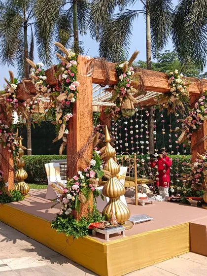 For a rustic-chic wedding, we designed this wooden mandap adorned with pastel roses and pampas grass. The hanging wicker baskets with florals add a unique, bohemian touch.