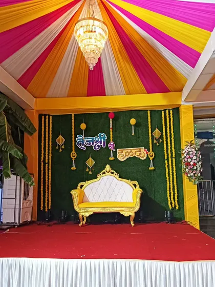 Here is a vibrant Haldi ceremony stage I put together. I used a combination of yellow, pink, and white fabric for the tent ceiling, a green backdrop for contrast, and traditional marigold flower hangings to complete the festive look.
