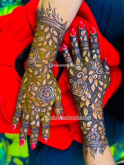 A vibrant red manicure pops against the dark, leafy henna stain.