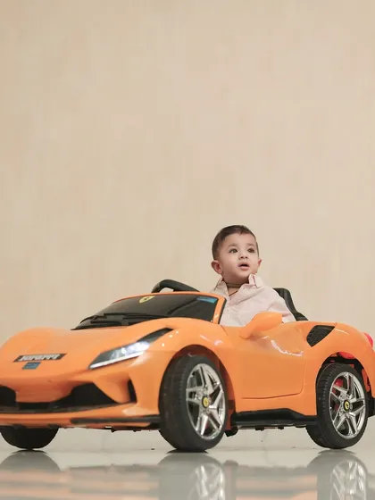 A future race car driver in the making. This little boy looks ready for action in his bright orange toy sports car.