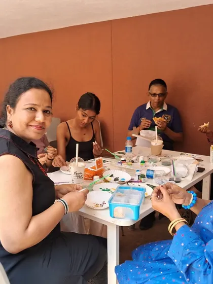 A candid moment from one of our interactive art classes. Participants are gathered around a table, sharing supplies and conversation as they work on their individual projects in a relaxed, communal setting.