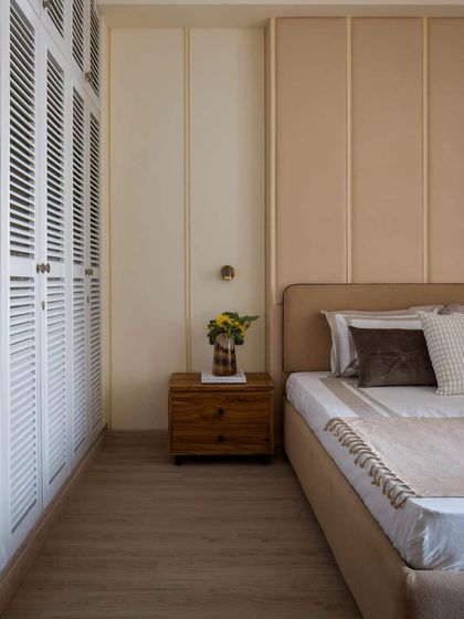 A bedroom in Hikari House, featuring a calm, neutral palette. The louvered wardrobe doors and upholstered wall panels add texture and a sense of quiet luxury to the compact space.