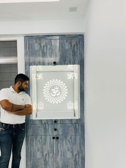 A modern mandir unit with a grey textured laminate finish and a backlit Corian panel featuring an 'Om' and 'Swastik' design.