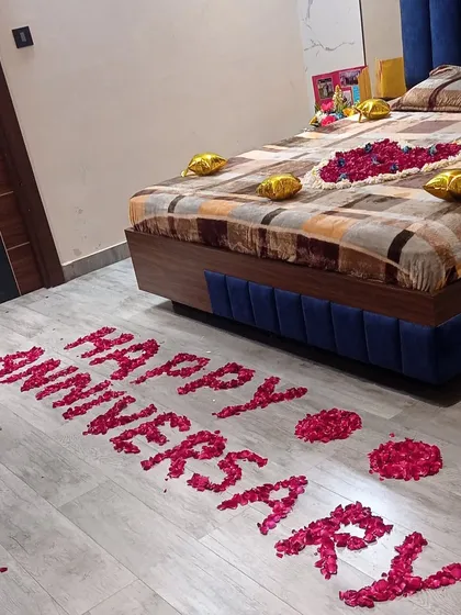 For this anniversary celebration, I spelled out 'HAPPY ANNIVERSARY' on the floor using fresh red rose petals. The bed is also decorated with a floral centerpiece and gold foil balloons to complete the surprise.