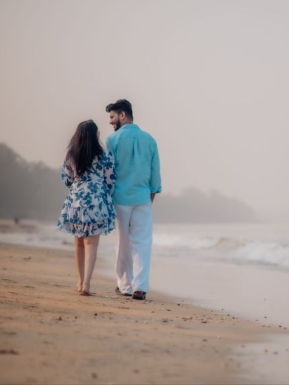 A quiet walk along the shore at dusk. This photo captures a serene, candid moment as the couple walks hand-in-hand, with the gentle waves and misty background creating a romantic atmosphere.