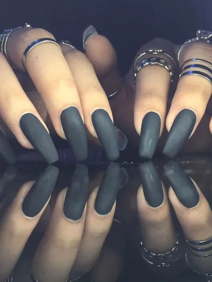 A close-up of the striking matte black manicure, styled with silver rings.
