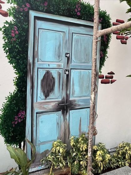 A close-up of the painted rustic blue door, which includes a real plant and tree to blend the 2D art with 3D reality.