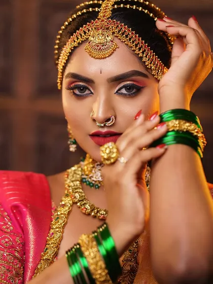 A powerful bridal portrait showcasing bold, artistic makeup. The sharp winged eyeliner and vibrant red lip are balanced with traditional jewellery, creating a look that is both fierce and classic.
