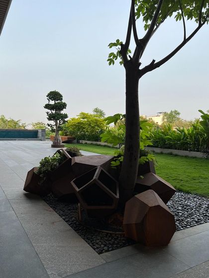 A cluster of Corten steel "rocks" that double as planters, surrounding the base of a tree. This custom-designed feature blends sculptural form with function, adding a raw, industrial texture to the landscape.