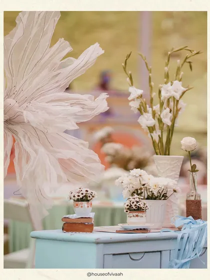 A detail shot of a tablescape, featuring a giant ethereal paper flower and simple arrangements in textured vases, adding an artistic and delicate touch to the Haldi lunch.