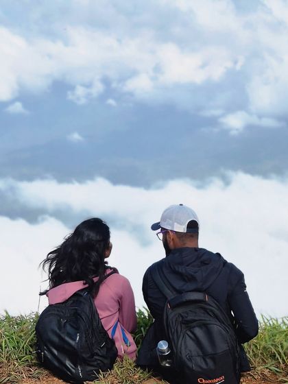 A couple sits together, looking out at the sky full of clouds from a viewpoint on the Bandaje trek.