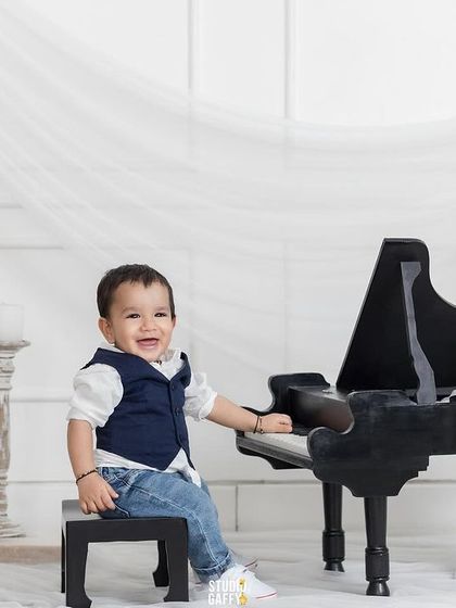 A dapper little gentleman playing a mini grand piano in a classic white set.