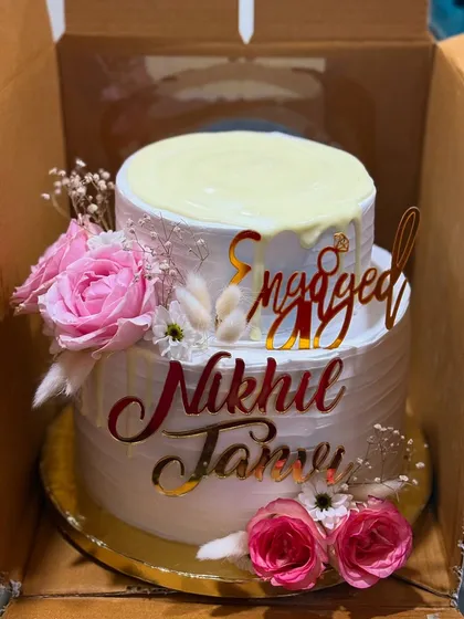 A close-up of the two-tier engagement cake, highlighting the custom acrylic toppers and delicate flowers.