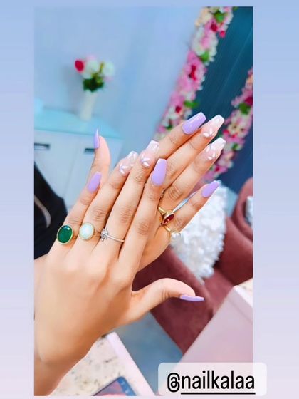 A beautiful set of long, coffin-shaped nails in a solid lavender color, with accent nails featuring encapsulated white flowers.