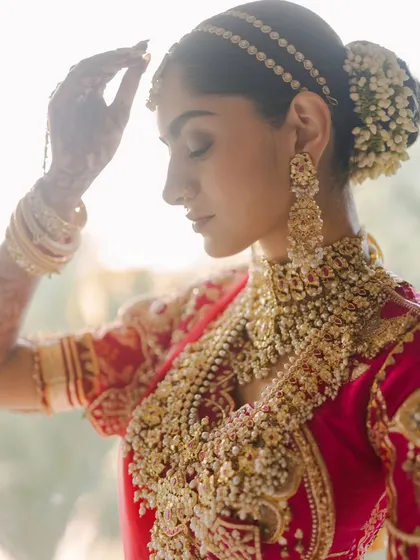 A serene portrait of the bride. The soft, natural light highlights the intricate details of her jewelry and the delicate flowers in her hair, a moment of calm before the ceremony.