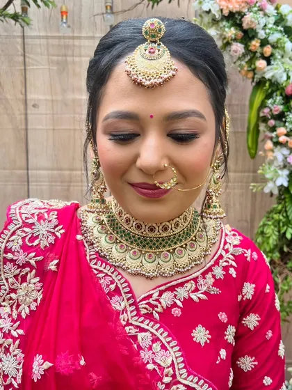 A close-up of the final look. The eye makeup is soft yet defined, the skin is glowing, and the lip color perfectly complements her red lehenga and green jewelry.