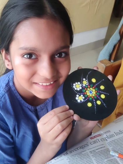 This young artist proudly displays her dot painting, which features a delicate floral-inspired mandala. It’s amazing to see the detailed work that children can produce when given the right tools and encouragement.