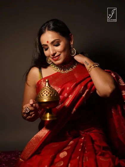 A festive-themed shot with a model in a vibrant red saree, holding a traditional brass incense burner. The warm lighting creates a devotional and serene mood.