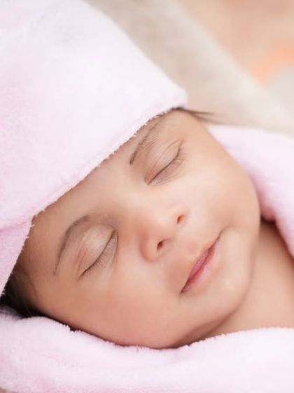 A peaceful close-up of a newborn's face, sleeping soundly in a soft pink robe and head wrap. This shot focuses on the serene and angelic expression of a sleeping baby.