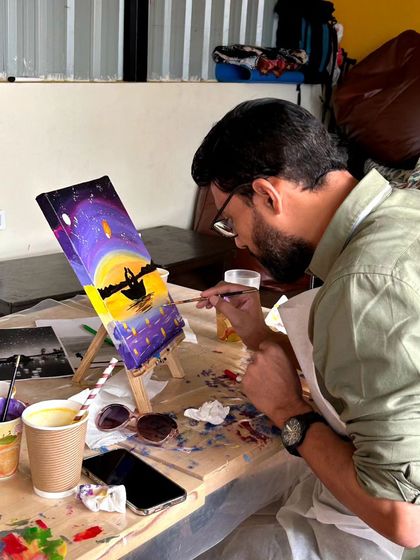 A participant focused on adding details to his sunset boat scene. The cozy atmosphere of the cafe makes for a perfect painting environment.