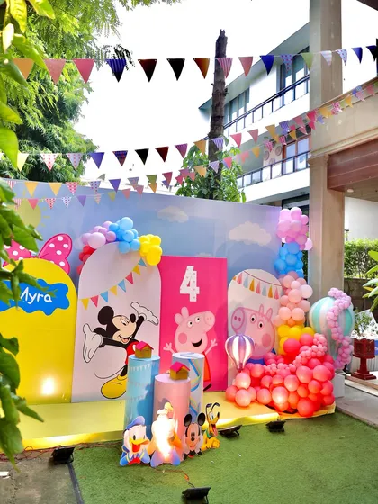An outdoor party scene featuring colorful backdrops with Mickey Mouse and Peppa Pig. The festive bunting and balloon decorations complete this cheerful and fun-filled setup.