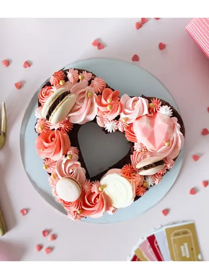 A timeless symbol of love, personalized just for you. This heart-shaped monogram cake, decorated with pink rosettes and macarons, is perfect for a romantic celebration.