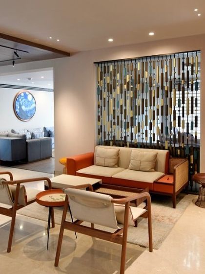 A casual seating area featuring mid-century modern inspired chairs and a vibrant orange sofa. A decorative screen made of wood and metal adds texture and visual interest while subtly dividing the space.