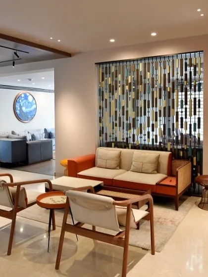 A casual seating area featuring mid-century modern inspired chairs and a vibrant orange sofa. A decorative screen made of wood and metal adds texture and visual interest while subtly dividing the space.