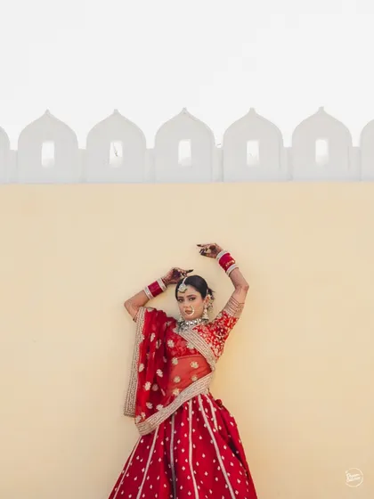 A striking, high-fashion pose from the bride in her traditional red lehenga against a minimalist yellow wall in Udaipur.