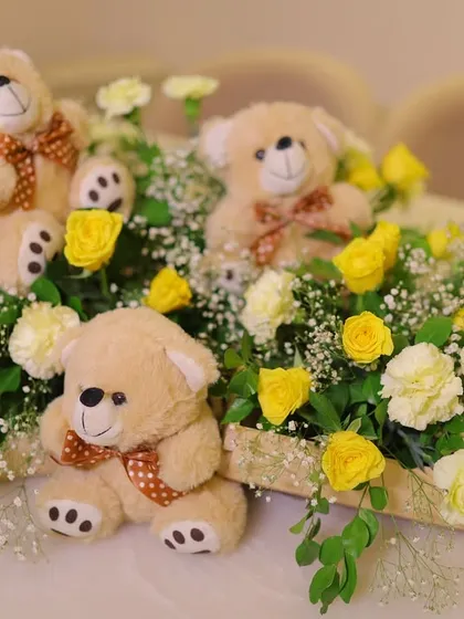 A sweet centerpiece for a baby shower, featuring three adorable teddy bears nestled in a bed of yellow and white flowers.