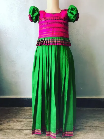 Here is another colour combination for a kids' Paavada blouse, with a pink top and a solid green skirt. The peplum design and puff sleeves are stitched for a very good fit.