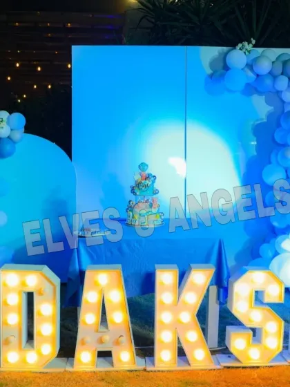 The cake-cutting stage for Daksh's birthday, featuring a clean blue backdrop, balloon arch, and his name in large marquee letters.