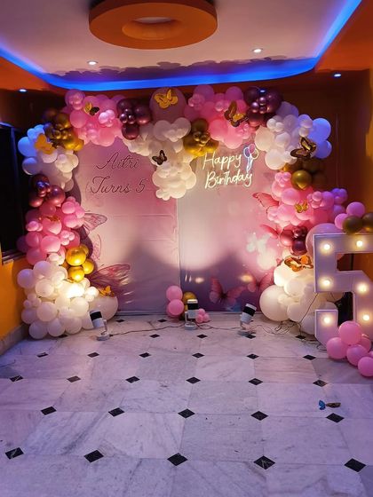 A beautiful butterfly and fairy theme for a 5th birthday, using a soft pink and white color palette, a large balloon arch, and a light-up marquee number.